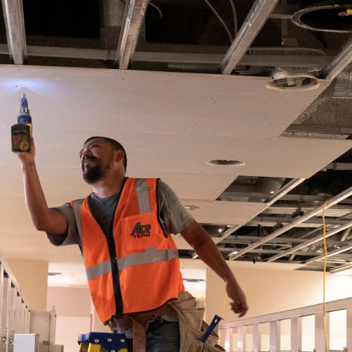 A worker in an orange vest installing drywall